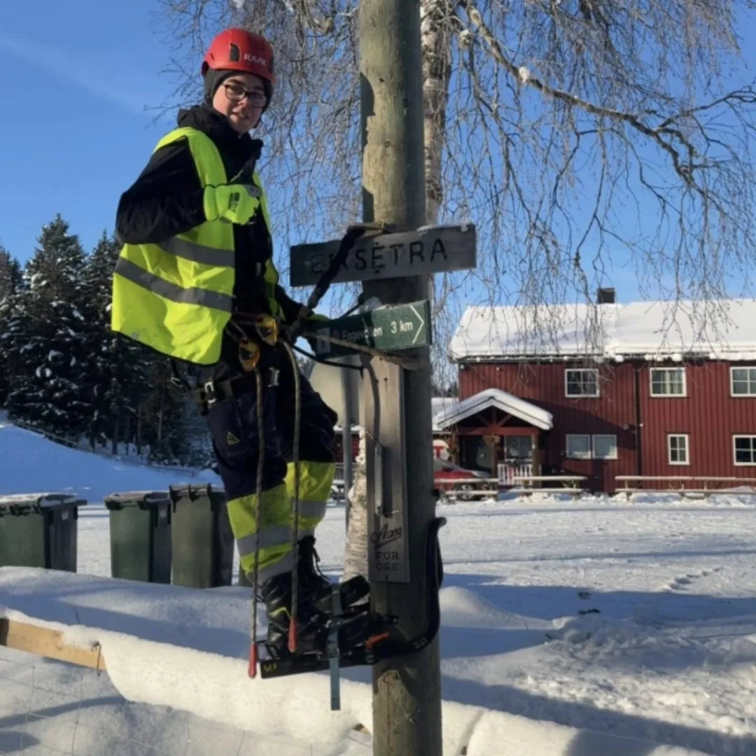 Montør i en stolpe ved et rødt hus i snøen